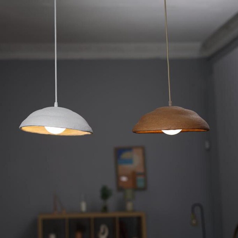 May include: Two hanging pendant lights with white and brown paper shades. The lights are turned on and illuminate the room.