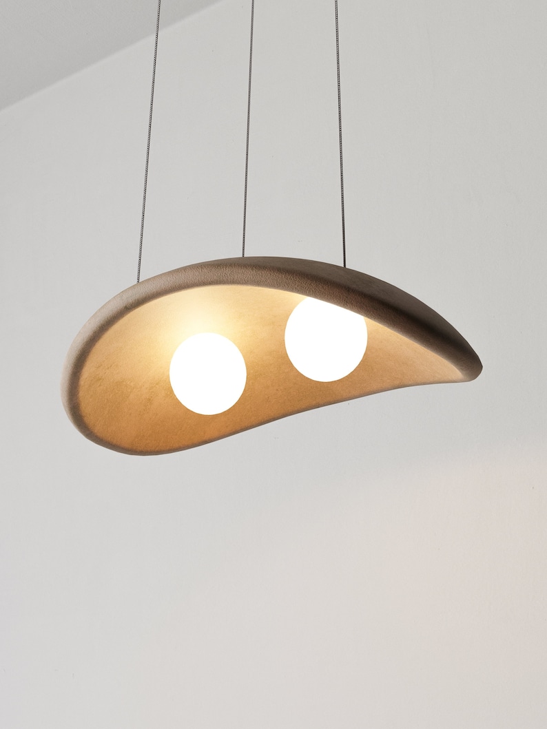 May include: A modern pendant light fixture with a brown, curved, ceramic shade and two white globe light bulbs.