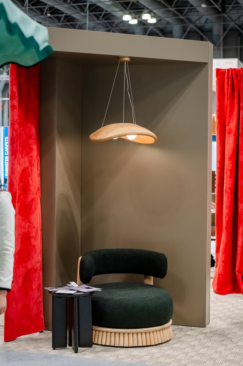 May include: A black and green upholstered armchair with a wooden base sits in a room with a wooden ceiling and red curtains. A wooden pendant light hangs above the chair.