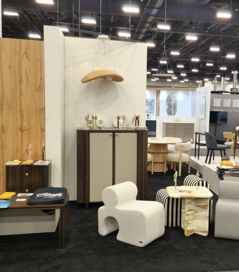 May include: A white, fluffy, modern chair with a unique shape sits in a room with a wooden cabinet, a striped chair, and a table with a patterned top. The room has a white wall with a brown wooden panel behind the cabinet.