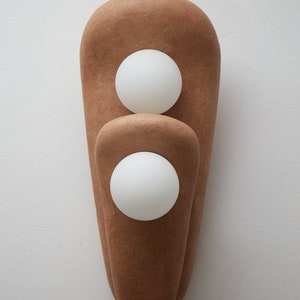 May include: A brown wall sconce with two white globe light bulbs. The sconce is made of a textured material and has a unique, organic shape.