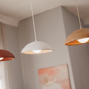Pode incluir: Tr&ecirc;s lumin&aacute;rias pendentes com design moderno. As c&uacute;pulas s&atilde;o em tons de marrom, branco e ferrugem, cada uma com uma luz quente e brilhante. As luzes pendem do teto com cabos finos, criando uma est&eacute;tica minimalista.