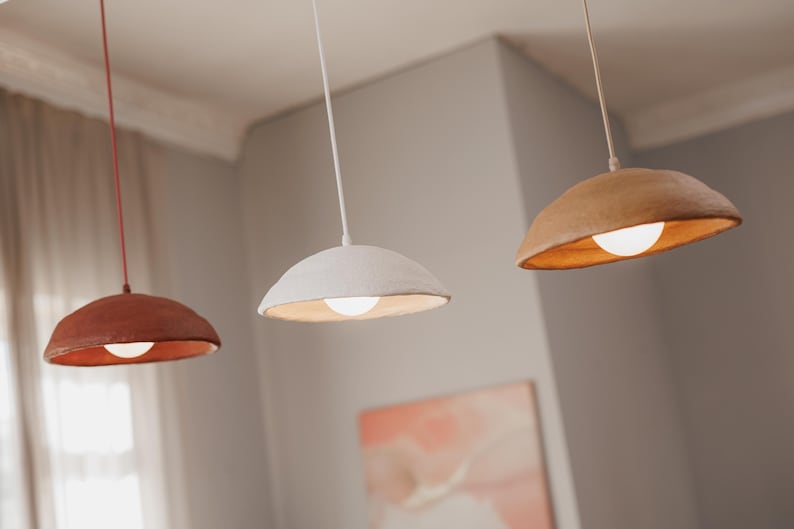 Pode incluir: Tr&ecirc;s lumin&aacute;rias pendentes com design moderno. As c&uacute;pulas s&atilde;o em tons de marrom, branco e ferrugem, cada uma com uma luz quente e brilhante. As luzes pendem do teto com cabos finos, criando uma est&eacute;tica minimalista.