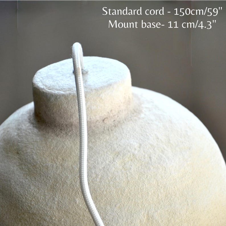 May include: Close-up of a beige pendant light fixture with a white cord. The fixture has a textured surface and a rounded shape. The cord is 59 inches long, and the mount base is 4.3 inches.