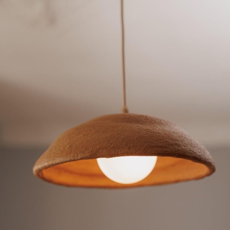 May include: A brown, round, felt pendant light fixture with a white light bulb hanging from the ceiling.