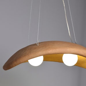 May include: A modern, curved wooden pendant light fixture with two white globe light bulbs.