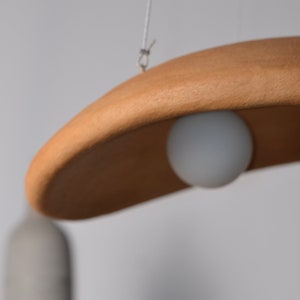 May include: A wooden pendant light fixture with a white globe light bulb hanging from a white cord.