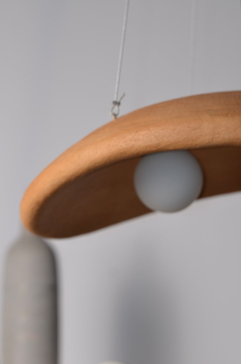 May include: A wooden pendant light fixture with a white globe light bulb hanging from a white cord.