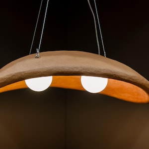 May include: A terracotta-colored pendant light fixture with two white globe light bulbs. The fixture is shaped like a crescent moon and hangs from a ceiling.