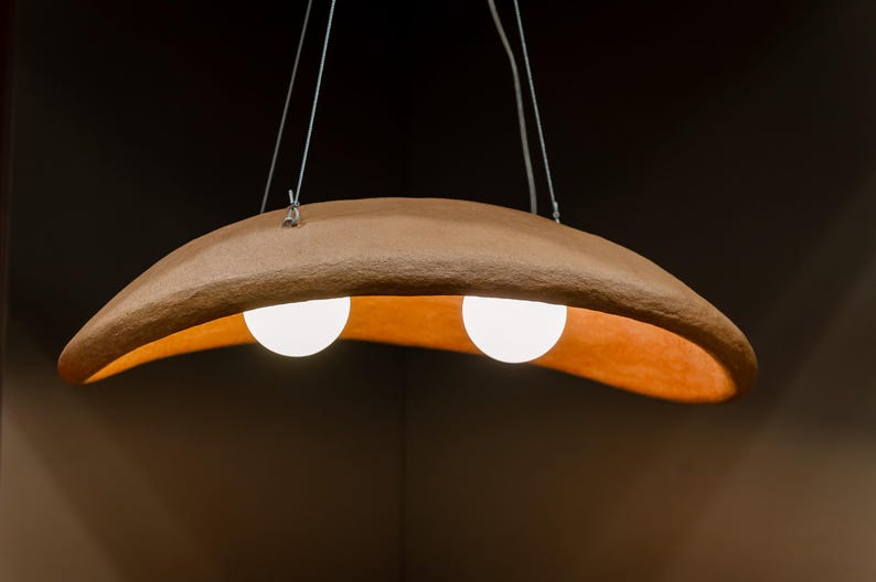 May include: A terracotta-colored pendant light fixture with two white globe light bulbs. The fixture is shaped like a crescent moon and hangs from a ceiling.