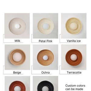 May include: A color chart titled Our Colours displaying eight circular wall lamps in Milk, Petal Pink, Vanilla ice, Beige, Ochra, Terracotta, Red, and Graphite. Each lamp features a central white light bulb. Text states Custom colors can be made per request.