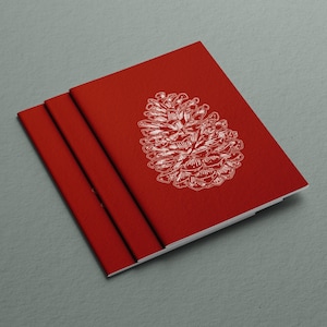 Może przedstawiać: Trzy czerwone zeszyty ułożone jeden na drugim. Górny zeszyt ma białą ilustrację szyszki na przedniej stronie.