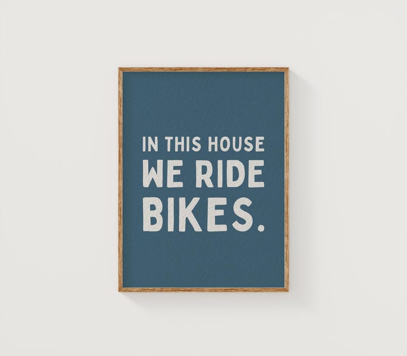 May include: A blue framed print with the text "In this house we ride bikes." in white lettering.