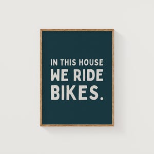 May include: A dark blue framed print with white text that reads "In this house we ride bikes."