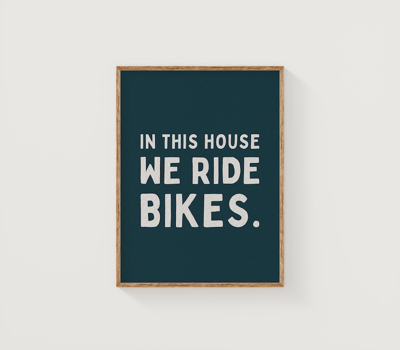 May include: A dark blue framed print with white text that reads "In this house we ride bikes."