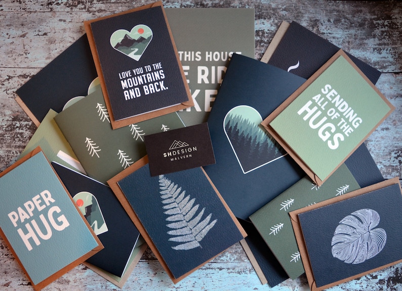 May include: A collection of greeting cards with various designs, including a mountain range, a fern, and a monstera leaf. The cards are all in shades of green and black with white text. The text on the cards includes "Love you to the mountains and back", "Sending all of the hugs", and "Paper hug".