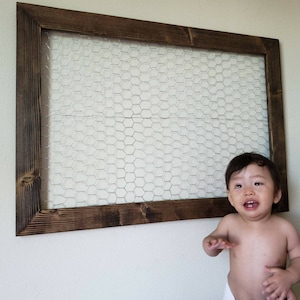 May include: A brown wooden frame with a wire mesh insert. A young child is standing in front of the frame.