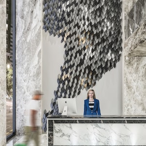A sleek office reception area showcasing a contemporary waiting desk placed in front of a textured accent wall built with 3D Mabel copolymer tiles.