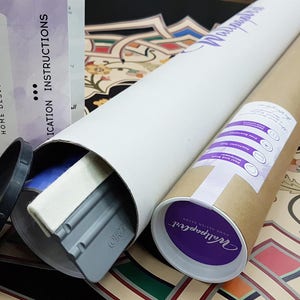 May include: A brown cardboard tube with a purple label that says "Wallpaper Art" and a white label with instructions for applying wallpaper. The tube is lying on a colorful patterned surface.