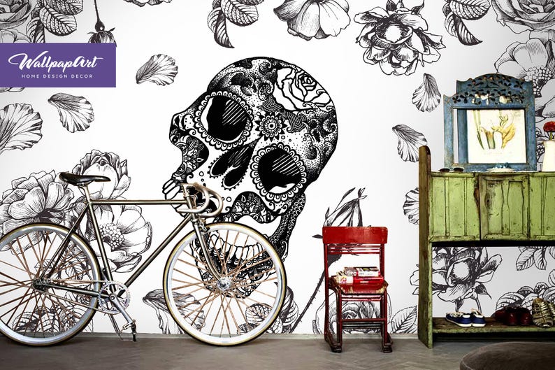 May include: Black and white illustration of a skull with floral details on a white background. A bicycle, a red chair, and a green cabinet with a mirror are in the foreground.