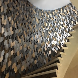 A modern architectural stairwell featuring a continuous, textured wall made of MABEL 3D geometric panels, creating a flowing, modern accent that follows the ascent of the stairs.