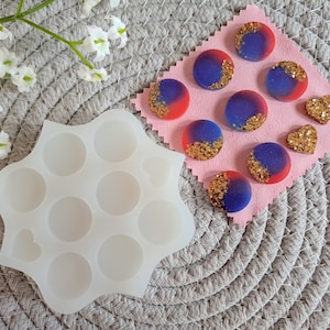 May include: A white silicone mould with nine round cavities and one heart-shaped cavity. The mould is designed for making resin crafts.  A pink fabric surface with eight round resin pieces and two heart-shaped resin pieces.