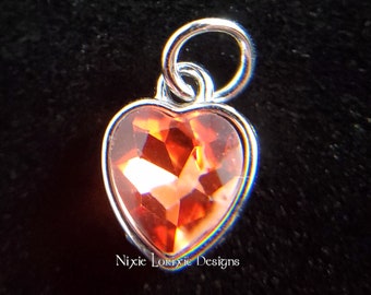 May include: A silver charm with a heart-shaped orange crystal. The charm has a loop at the top for attaching to a bracelet or necklace.