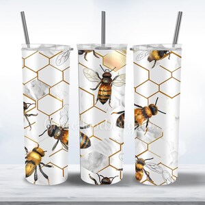 Puede incluir: Tres vasos de acero inoxidable con fondo blanco y un patrón de panal de abeja dorado y abejas. Los vasos son todos del mismo tamaño y tienen una pajita.