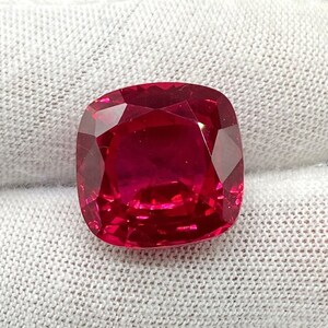 May include: A vibrant red cushion-cut gemstone with a smooth, polished surface.