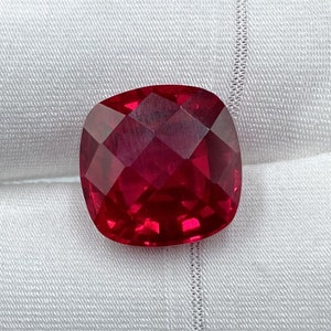 May include: A deep red cushion-cut gemstone with many facets.