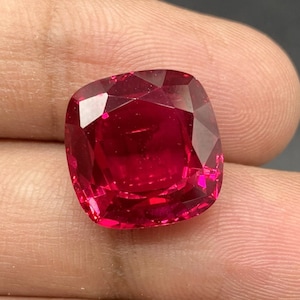 Puede incluir: Una piedra preciosa de talla cojín de color rojo intenso con un alto pulido.