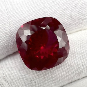 Puede incluir: Una piedra preciosa de color rojo intenso de talla cojín con una superficie facetada.