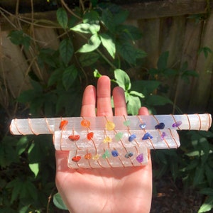 Peut inclure: Trois baguettes de sélénite enveloppées de fil de cuivre et ornées de pierres précieuses colorées. Les pierres précieuses sont disposées en arc-en-ciel, représentant les sept chakras.