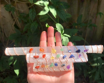 May include: Three selenite wands wrapped with copper wire and adorned with colorful gemstones. The gemstones are arranged in a rainbow pattern, representing the seven chakras.