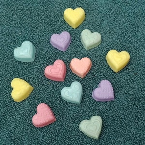May include: Assortment of pastel-colored heart-shaped soaps. The soaps are arranged on a green towel. The soaps are in shades of pink, yellow, blue, and green.