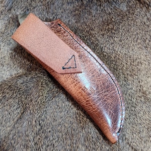 May include: A brown leather knife sheath with a triangle design and stitching. The sheath has a flap that folds over the knife.