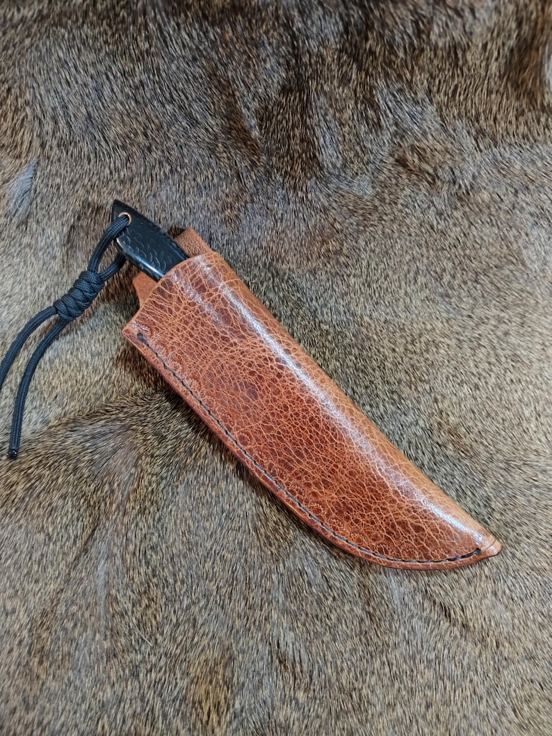 May include: A brown leather sheath with a black knife inside. The sheath has a knotted cord attached to it.