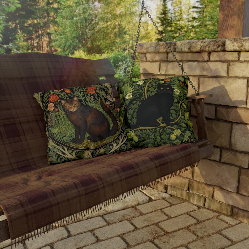 May include: Two decorative throw pillows with cat illustrations. One pillow features a brown cat in a floral design, the other a black cat. The pillows are on a brown plaid swing, with a brick wall and greenery in the background.