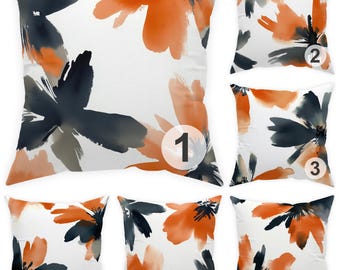 Könnte beinhalten: Quadratische weiße Kissen mit einem Aquarell-Blumenmuster. Die Blumen sind in Orange-, Marineblau- und Grautönen gehalten. Diese Kissen sind ein dekoratives Element für ein Sofa oder Bett.