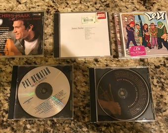 Op de afbeelding: Vijf cd's in jewelcases worden getoond. De artiesten zijn Chris Isaak, James Taylor, Len, Pat Benatar en Ozzy Osbourne. De hoesjes zijn zwart en de cd's zijn zichtbaar. De afbeelding toont een verzameling muziekalbums.