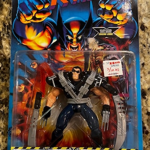 May include: X-Men Battle Brigade Wolverine action figure in original packaging. The figure is in a plastic bubble, with a blue and yellow background. The packaging includes the text "Battle Brigade" and "Total Assault Arsenal".