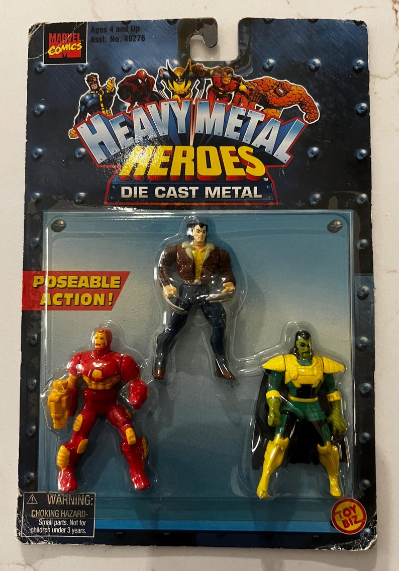 May include: A sealed package of "Heavy Metal Heroes" die-cast metal action figures. The package features three figures: Iron Man in red and gold, a figure in brown and blue, and a green and yellow figure. The package has the Marvel Comics logo.