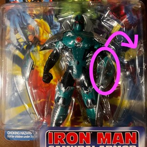May include: A green and silver action figure of Iron Man in Samurai Armor. The figure has a red eye and a silver sword. The packaging says "Iron Man Samurai Armor".