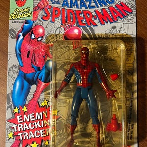 May include: A red and blue action figure of Spider-Man with a spring-loaded web shooter. The figure is packaged in a plastic blister pack with a cardboard backing. The packaging features a comic book style illustration of Spider-Man and the text "The Amazing Spider-Man".