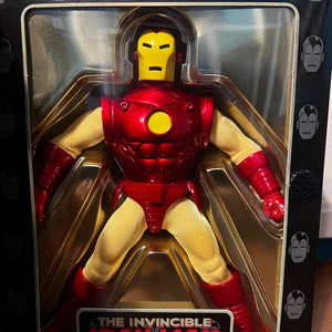 May include: A red and yellow action figure of Iron Man in a clear plastic box. The box has a black background with a repeating pattern of Iron Man's face. The box has the text "The Invincible Iron Man" on the bottom.