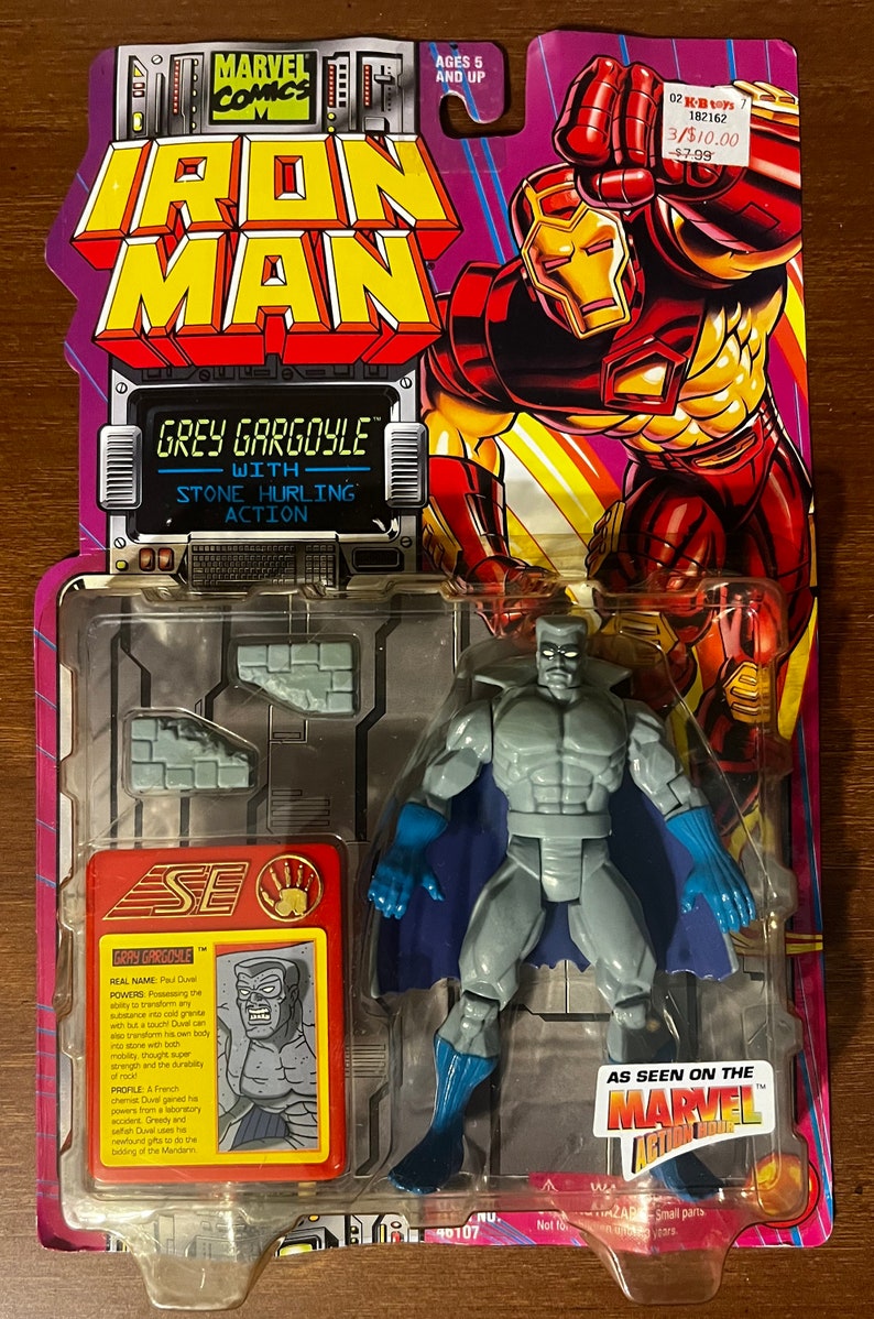 May include: A plastic action figure of Grey Gargoyle from the Marvel Comics universe. The figure is grey with a blue cape and is holding a stone in his right hand. The figure is packaged in a plastic blister pack with a red, white, and blue background. The packaging includes the Marvel logo and the words "As Seen on the Marvel Action Hour".