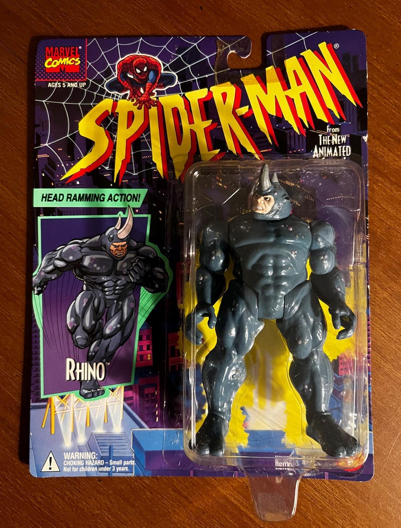 May include: A Spider-Man action figure of Rhino, from the animated series, in its original packaging. The figure is gray and blue, with a horn on its head. The packaging features the Marvel Comics logo, Spider-Man imagery, and the text "HEAD RAMMING ACTION!"