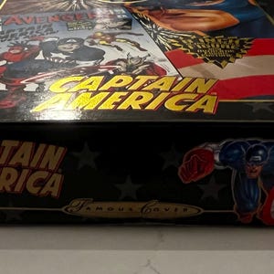 May include: Black box featuring Captain America graphics and text. The box has a comic book cover design with the words "Captain America" in gold lettering. A cartoon image of Captain America is on the side.