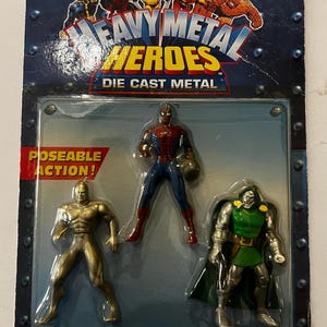 Pode incluir: Figuras de a&ccedil;&atilde;o de metal fundido "Heavy Metal Heroes" da Marvel Comics. A embalagem inclui tr&ecirc;s figuras: uma figura dourada, Homem-Aranha em vermelho e azul e Doutor Destino em verde e prata. A embalagem tem um aviso.