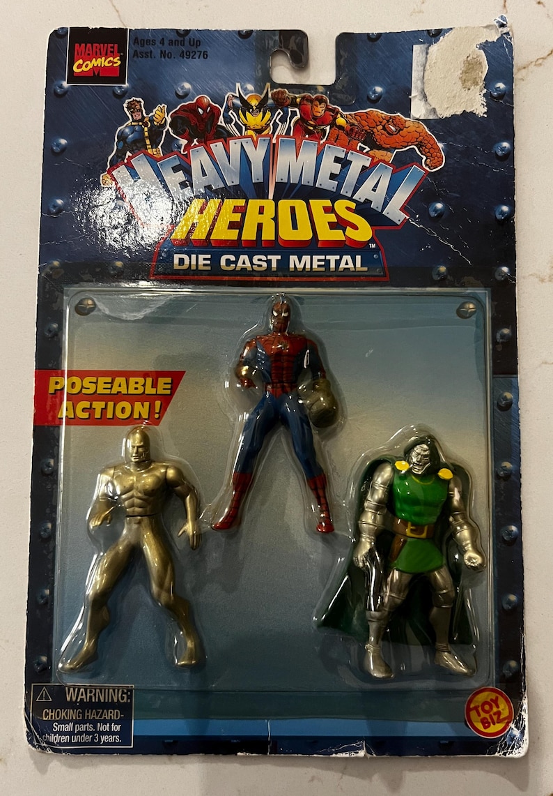 Pode incluir: Figuras de a&ccedil;&atilde;o de metal fundido "Heavy Metal Heroes" da Marvel Comics. A embalagem inclui tr&ecirc;s figuras: uma figura dourada, Homem-Aranha em vermelho e azul e Doutor Destino em verde e prata. A embalagem tem um aviso.